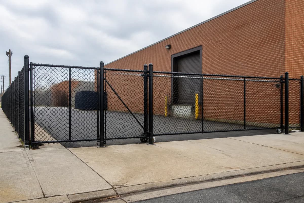 Black-coated commercial chain-link perimeter and vehicle gate at a brick warehouse